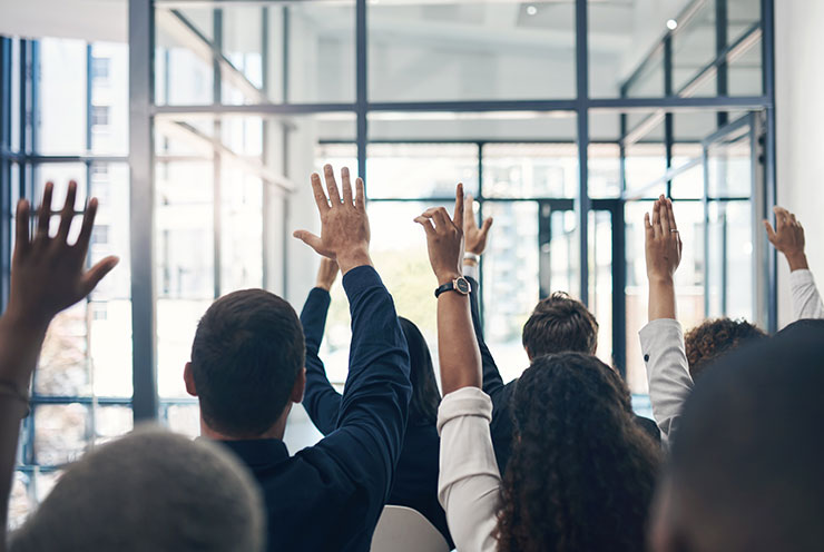 Shot of a group of businesspeople raising their hands during a presentation
