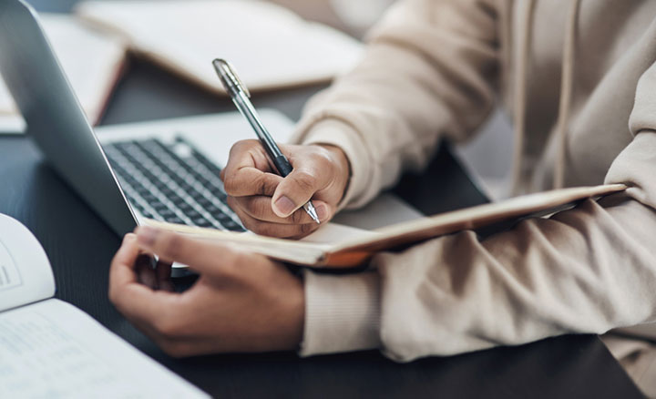 Shot of an unrecognisable man writing in a notebook while working from home